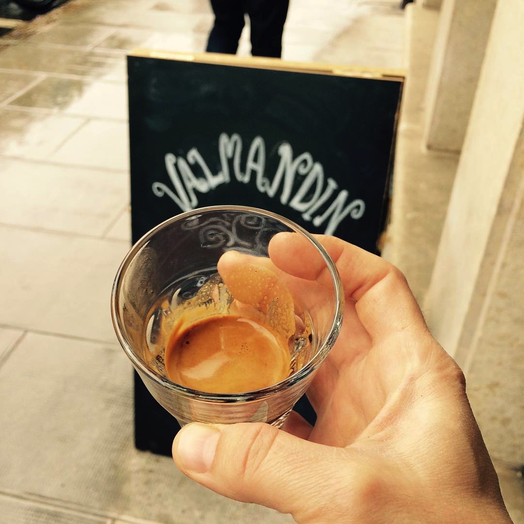 A glass cup with freshly brewed Valmandin espresso surrounded by the handwritten Valmandin sign.